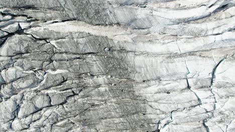 top-down-view-of-ice-glacier-in-the-mountains-with-deep-black-crevasses-and-crack,-melting-glacier-in-switzerland-due-to-global-warming