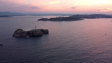 Aerial-dramatic-sunset-above-Santander-city,-drone-rotate-around-lighthouse-island-panoramic-view-of-all-the-bay-with-beach-and-harbor