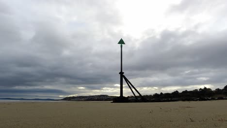 Timelapse-overcast-storm-clouds-passing-above-metal-high-tide-marker-on-sandy-beach-coastline