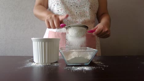 Latin-woman-wearing-an-apron-preparing-cooking-baking-a-cake-sieving-the-flour-with-a-metal-strainer-and-her-hand