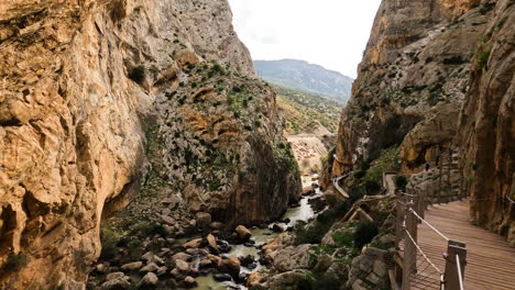 4k-Aufnahme-Von-Touristen,-Die-Auf-Einem-Holzpfad-Zwischen-Klippen-Mit-Gebirgsfluss-Unter-El-Caminito-Del-Rey-In-Der-Schlucht-Chorro,-Provinz-Malaga,-Spanien,-Spazieren