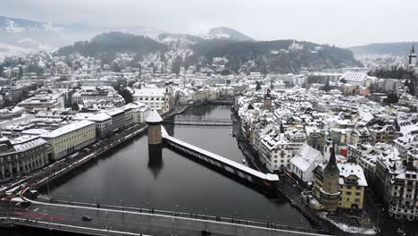 Aerial-flyover-towards-Kappelbrücke-in-Lucerne,-Switzerland-as-the-city-is-covered-in-snow-in-winter