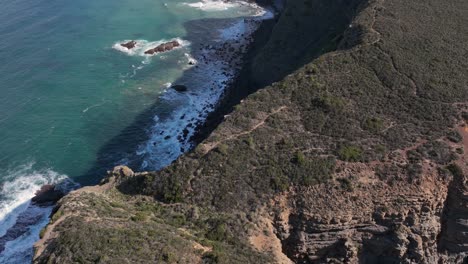 Aerial-tilt-shot-of-rugged-sunlit-cliffs-in-a-secluded-bay-along-the-ocean