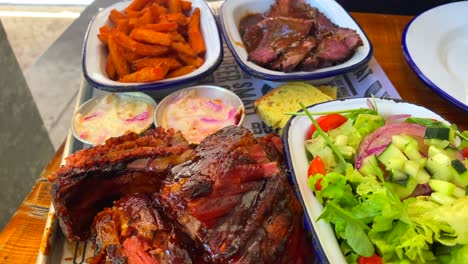 Dynamic-shot-of-beef-brisket-with-salad,-pork-ribs-with-sweet-potato-fries,-cornbread-and-coleslaw,-traditional-american-food-in-a-restaurant,-4K