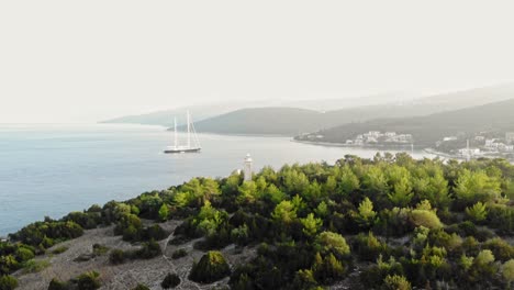 Lighthouse-of-Fiskardo-village---Boat-in-blue-sea-in-Kefalonia-island,-Greece---aerial-drone-shot