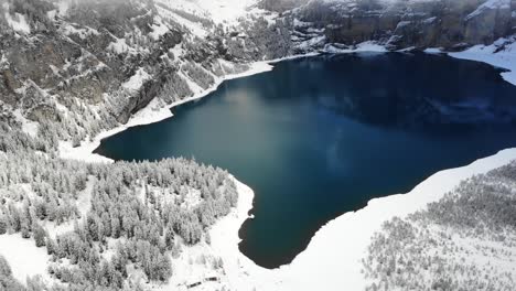 Sobrevuelo-Aéreo-Junto-A-Las-Orillas-Del-Lago-Oeschinensee-En-Kandersteg,-Suiza-En-Un-Día-De-Invierno-Con-Picos-Montañosos-Nubes-Ocultas