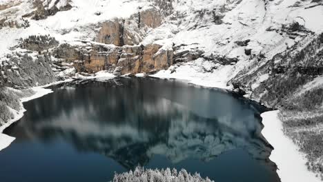 Aerial-view-of-lake-Oeschinensee-in-Kandersteg,-Switzerland-with-a-reflection-of-mountain-peaks-on-a-winter-day