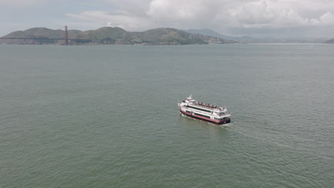 Aerial-rotating-shot-of-ferry-with-Golden-Gate-Bridge-in-background-in-San-Francisco,-CA