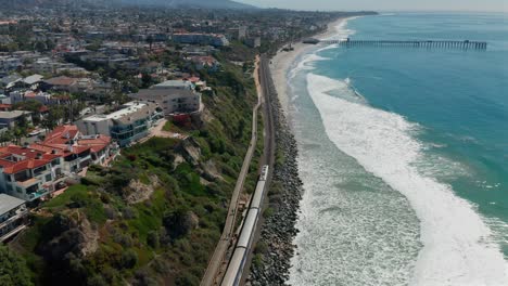 Aerial-view-of-oceanfront-housing-and-an-Amtrak-train-moving-towards-San-Clemente,-California