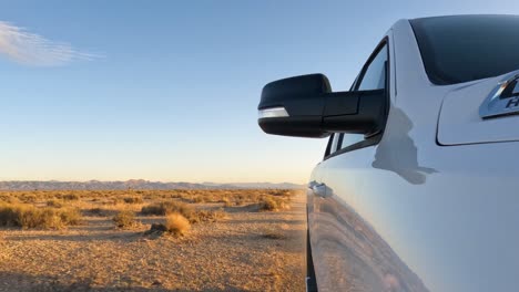 Driving-along-a-dusty-dirt-road-in-the-Mojave-Desert-with-a-view-of-the-side-of-the-truck-looking-back-at-the-arid-landscape-and-Joshua-trees
