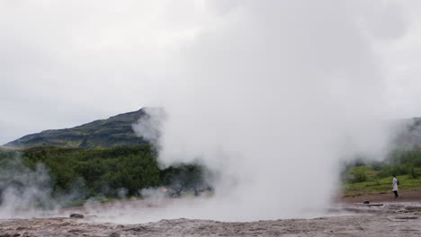 Unrecognizable-tourists-watching-a-geyser-erupting-water,-Iceland