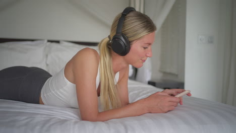 Woman-swaying-head-to-rhythm-of-music-while-relaxing-in-comfy-bed,-scrolling-phone