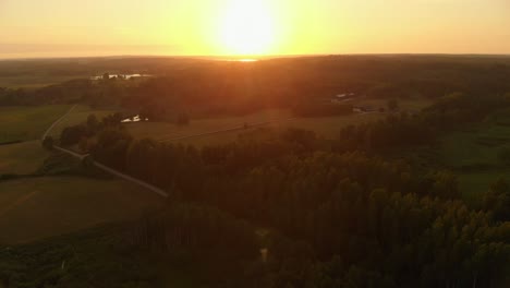 Golden-sunset-over-landscape-of-agriculture-and-forest,-aerial-view