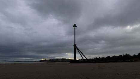 Overcast-stormy-clouds-pass-above-metal-high-tide-marker-on-sandy-beach-coastline-timelapse