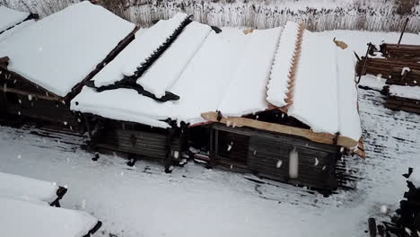 Snow-covered-rooftops-of-wooden-historic-buildings-in-Latvia-during-snowfall,-aerial-drone-view