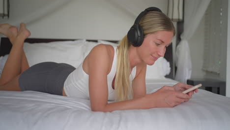 Mujer-Escuchando-Música-En-Spotify-A-Través-De-Un-Smartphone,-Relajándose-En-El-Concepto-De-Cama