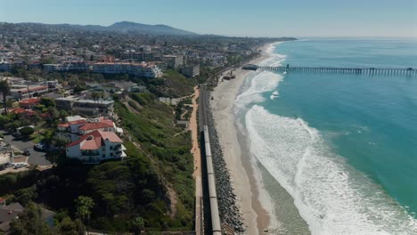 Aerial-view-of-an-Amtrak-train-moving-along-side-the-Pacific-Ocean-near-San-Clemente,-California