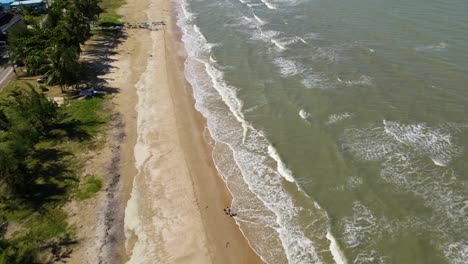 Eine-Luftaufnahme,-Die-Einen-Strand-Zeigt,-Wellen,-Die-Wildwasser-Machen,-Zwei-Menschen,-Die-Am-Strand-Spazieren-Gehen