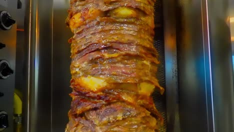 Continuous-Loop-4-of-5-closeup-of-stacked-steaks-thinly-sliced-onto-a-vertical-stainless-steel-spit-BBQ-marinated-the-juices-flowing-downward-with-the-many-Arabic-herbs-used-in-a-slow-cooking-rotation