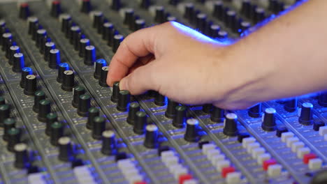 A-sound-engineer-music-producer-adjusting-the-audio-on-a-mixing-desk-turning-the-knobs-and-pressing-buttons