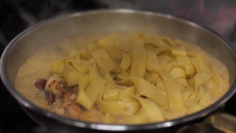 Fresh-boiled-pasta-added-to-frying-ragout-on-pan,-close-up
