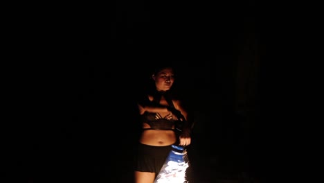 Asian-woman-spinning-blazing-hot-fire-ropes-from-front-to-to-back-in-night-time,-filmed-as-tight-medium-shot