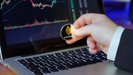 Businessman-flips-over-Ethereum-coin-in-his-fingers-whilst-looking-at-the-exchange-charts-and-prices-on-a-laptop