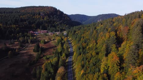Beautiful-aerial-view-of-a-hilly-mountain-landscape-surrounded-by-fall-foliage-forest-and-a-road-during-autumn-season