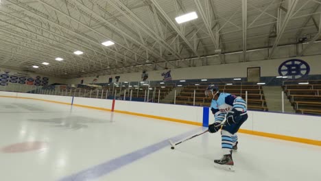 FPV-drone,-ice-hockey-player-stick-handling-puck-on-indoor-arena-ice-rink