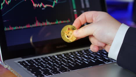Businessman-flips-over-doge-coin-in-his-fingers-whilst-looking-at-the-exchange-charts-and-prices-on-a-laptop