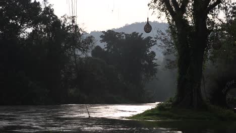 4k-De-Un-Río-Que-Fluye-Rodeado-De-Bosques-Durante-Un-Amanecer-Matutino-En-Phectahaburi,-Tailandia