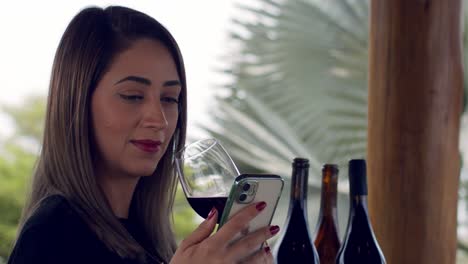 cinematic-shot-of-a-lady-sitting-in-a-tropical-garden-with-a-glass-of-red-wine-in-her-hand-looking-at-her-smartphone---close-up-slow-motion