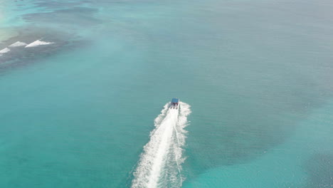 A-large-luxury-powerboat-cruises-parallel-along-white-sand-beaches-off-Sana-Island,-aerial-orbit
