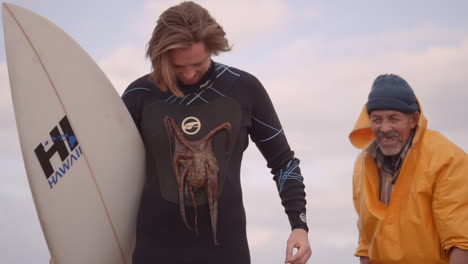 Moroccan-fisherman-sticks-octopus-to-a-tourist-surfer's-wetsuits,-all-smile