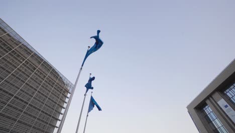 Close-skyline-view-of-European-flags-dancing-in-the-wind-against-the-Berlaymont-building-and-Europa-building-in-Brussels,-Belgium