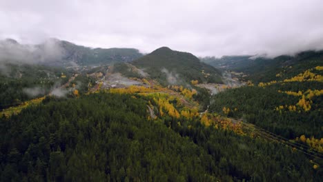 Cinematic-Drone-shot-Reveal-of-Foggy-Forest-Mountain-in-Fall-with-yellow-trees-Evergreens-and-rolling-Clouds-flyover