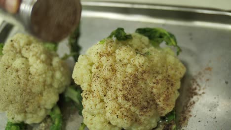 Unrecognizable-chef-sprinkling-cauliflower-heads-with-spices-before-baking,-close-up
