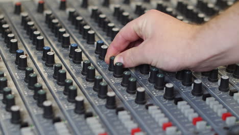 A-sound-engineer-music-producer-in-recording-studio-adjusting-the-audio-on-a-grey-mixing-desk-turning-the-knobs-and-pressing-buttons