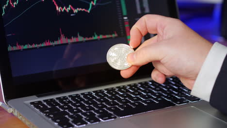 Businessman-flips-over-cardarno-coin-in-his-fingers-whilst-looking-at-the-exchange-charts-and-prices-on-a-laptop