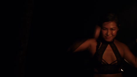 Asian-woman-spinning-fireball-poi-in-various-styles-in-dark,-filmed-from-side-and-front-as-medium-close-up-shot