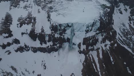 Snowy-Iceland-Mountains-with-Flowing-Waterfall-Cascading-off-Cliff---Aerial