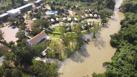 4K-Aerial-Drone-Footage-With-Dolly-Movement-Looking-Down-at-a-Hotel-Resort-Along-the-Riverside-in-Phetchaburi,-Thailand