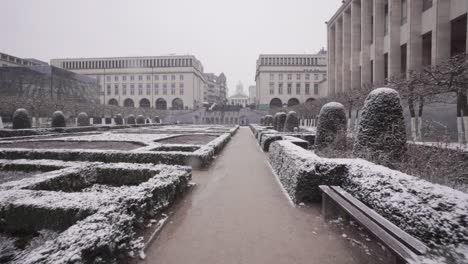 Slowly-moving-forward-in-the-beautiful-Mont-des-Arts-Gardens-in-Brussels,-Belgium-during-snowfall---Pov-tracking-shot