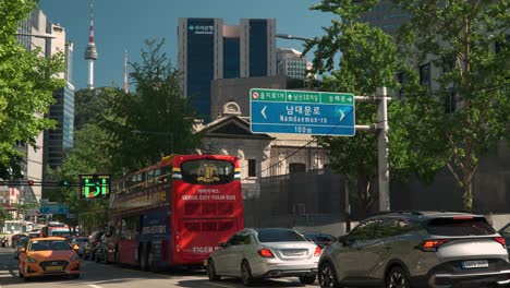 Doppelstöckiger-Roter-Seoul-City-Tour-Bus-Steckt-In-Einem-Stau-In-Der-Engen-Altstadtstraße-Auf-Der-Sogong-ro-Road-Mit-Blick-Auf-Den-Berühmten-N-Seoul-Tower-Oder-Den-Namsan-Tower-Im-Hintergrund