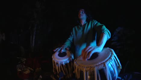 Musically-spiritual-moment-of-tabla-player-drumming-in-dark-outdoor-area-with-blue-key-light,-filmed-handheld-with-fish-eye-lens-in-slow-motion