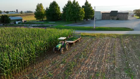 Children-on-John-Deere-tractor-and-wagon-harvest-corn-in-autumn-aerial-scene
