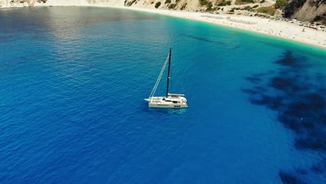 Aerial-View-of-Luxury-Sail-Yacht-in-Myrtos-Beach-with-blue-bay-on-Kefalonia-Island,-Greece---drone-shot