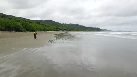 drone-aerial-video-in-nicaragua-beach,-san-juan-del-sur,-palm-,-managua,-rivas,-bicyclist-on-the-beach,-matagalpa,-central-america,-tourism