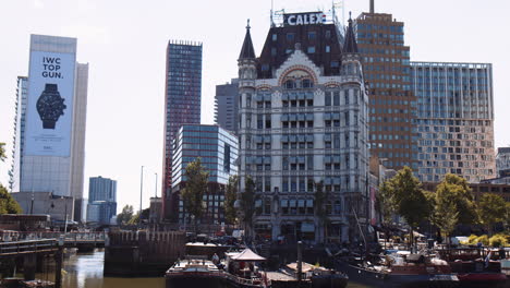 Tilting-shot-of-downtown-Rotterdam-with-boats-docked-at-the-port,-iconic-art-nouveau-Witte-Huis-building-in-background