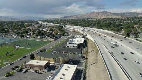 Highway-traffic-in-Lehi,-Utah-with-Silicon-Slopes-and-the-mountains-in-the-background---aerial-pull-back